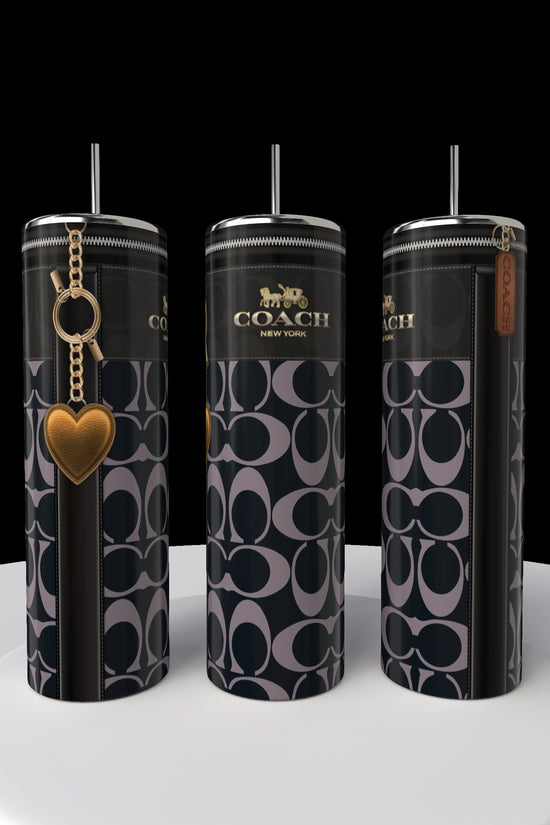 Three tall 20oz Coach Skinny Tumblers from Kreative Kreationz, featuring a black and gray pattern. Two have a heart charm and Coach tag. These stainless steel tumblers are elegantly displayed on a white circular platform against a black backdrop.