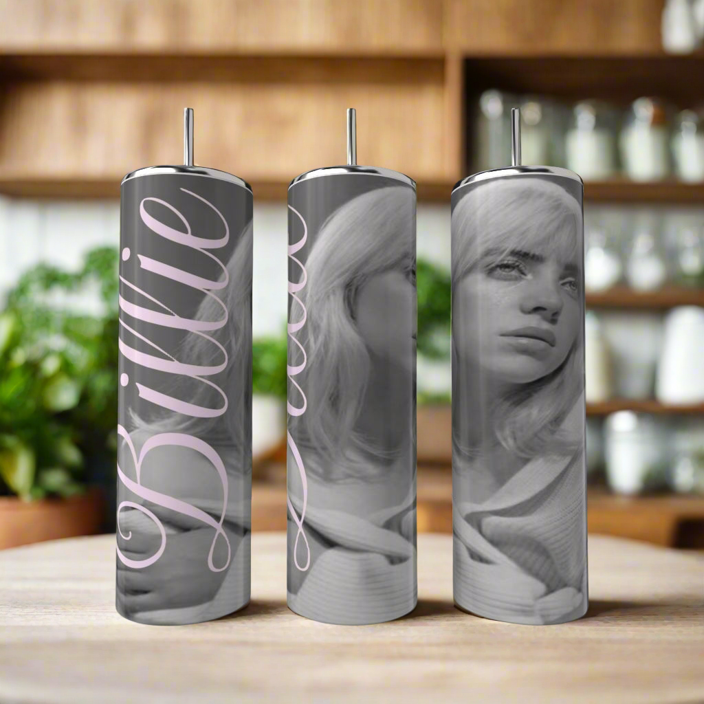 Three Kreative Kreationz Billie Ellish 20oz Tumblers, featuring black-and-white portraits of a woman and "Billie" script, sit on a wooden table. These eco-friendly, reusable tumblers add style and sustainability to your collection.