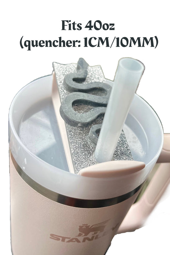 A close-up image shows a plastic straw with a silver glittery cover and snake-shaped decoration on a white Stanley tumbler lid topper. The text above the lid reads, 