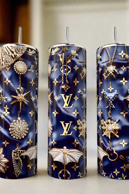 The Kreative Kreationz LV Blue & Gold 20oz Tumbler is a tall, navy eco-friendly luxury drinkware with silver straw, gold LV logo, and jewel-inspired star, moth & chain designs—an elegant choice for any kitchen counter.