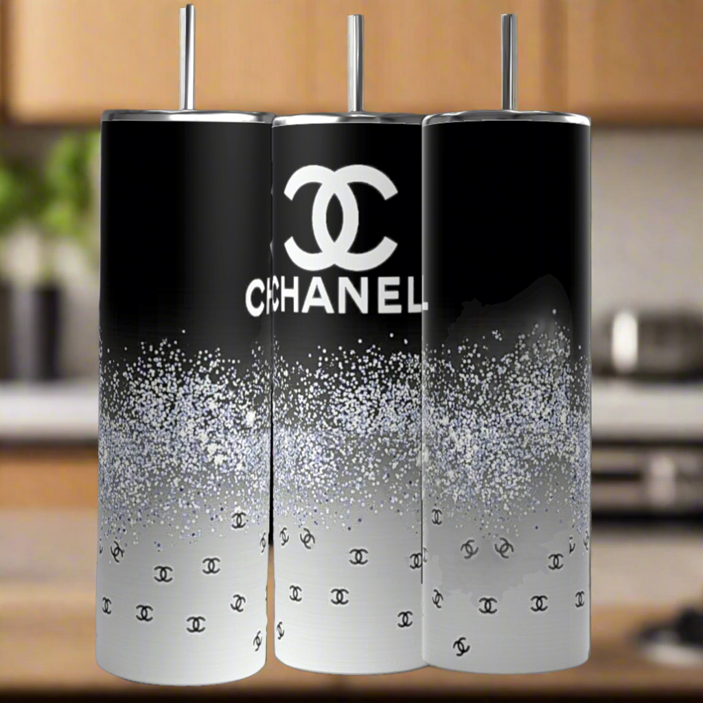 The Chanel | Black and Glitter 20oz Skinny Tumbler by Kreative Kreationz features a black-to-white gradient, sparkling glitter, and Chanel logos with silver straws—perfectly displayed in a stylish kitchen.