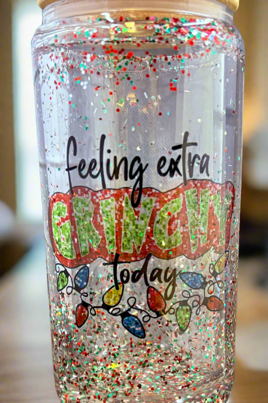 The Grinch Snowglobe Tumbler by Kreative Kreationz is a transparent 16oz jar with a bamboo lid, filled with red, green, and white glitter. It features the phrase 