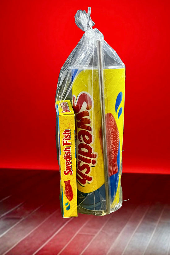 A plastic bag containing a Swedish Fish Gift Set with a 20oz stainless steel skinny tumbler, featuring yellow and blue packaging, branded 
