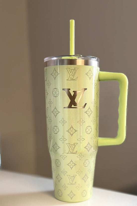 The LV Engraved Shimmer Tumbler by Kreative Kreationz is a large pale yellow stainless steel tumbler with a handle and straw, featuring the Louis Vuitton logo and monogram pattern, displayed on a light surface with a neutral background.