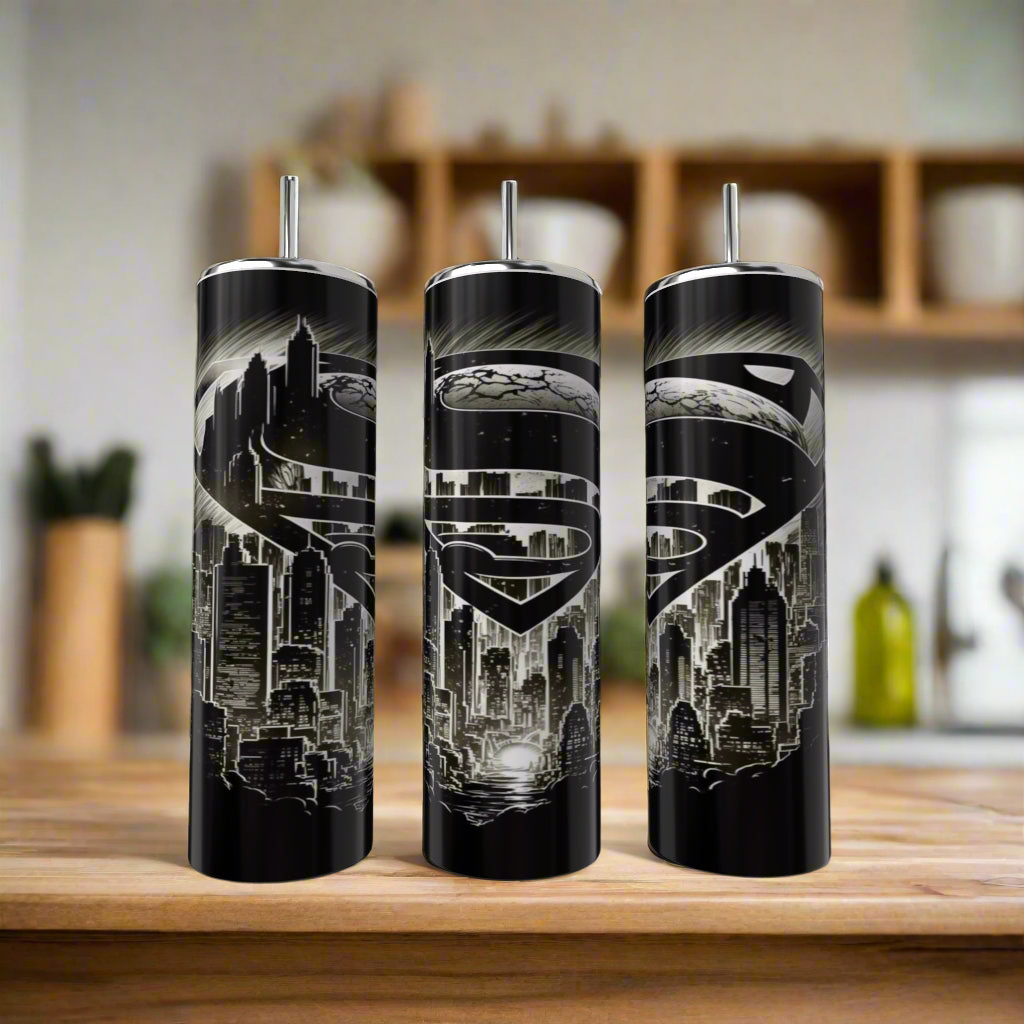 Three Kreative Kreationz Superman Modern 20oz Tumblers with black stainless steel, metallic Superman logos, and city skyline designs sit on a wooden counter with a blurred kitchen background—ideal for any fan.