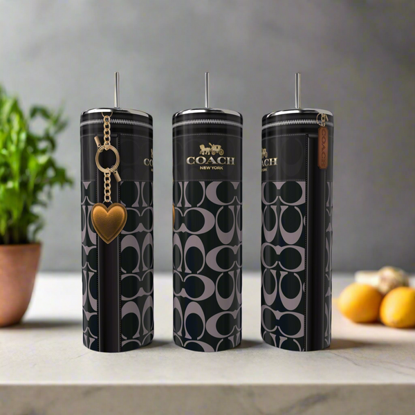 Three tall, cylindrical Coach 20oz Skinny Tumblers by Kreative Kreationz with black and gray signature patterns are on a kitchen counter; one features a gold heart keychain. A potted plant and lemons blur in the background.
