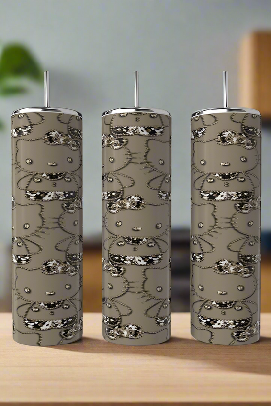 A Hello Kitty 20oz Tumbler by Kreative Kreationz sits on a wooden surface in a modern kitchen, accompanied by three tall, cylindrical soap dispensers and a green plant in the background.