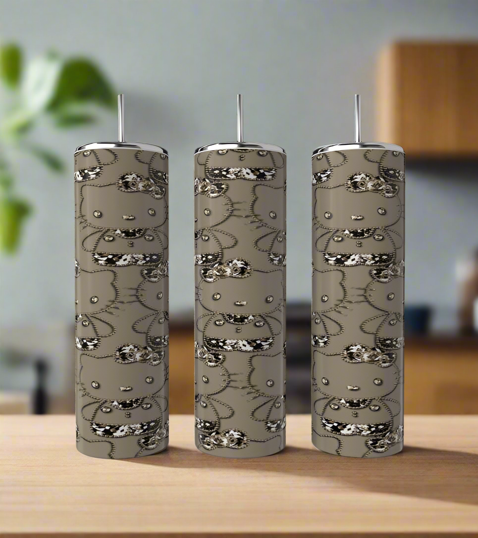 A Hello Kitty 20oz Tumbler by Kreative Kreationz sits on a wooden surface in a modern kitchen, accompanied by three tall, cylindrical soap dispensers and a green plant in the background.