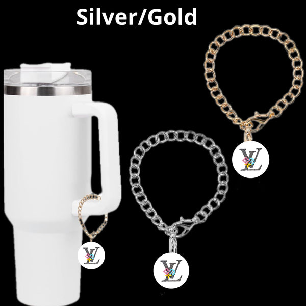 The Kreative Kreationz LV Charm Dangle features a white insulated tumbler adorned with a gold chain and a personalized pendant. Beside it are two lobster clasp chains, one gold and one silver, each with a round letter charm showcasing advanced electroplating technology.