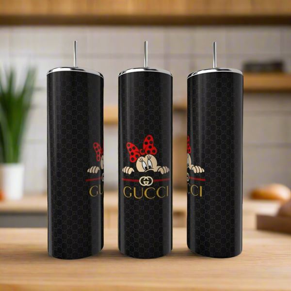 Three Gucci Mickey Mouse 20oz Skinny Tumblers by Kreative Kreationz rest elegantly on wood. Adorned with a cartoon character and red polka-dotted bow, they capture attention against a blurred kitchen backdrop dotted with plants and kitchenware.