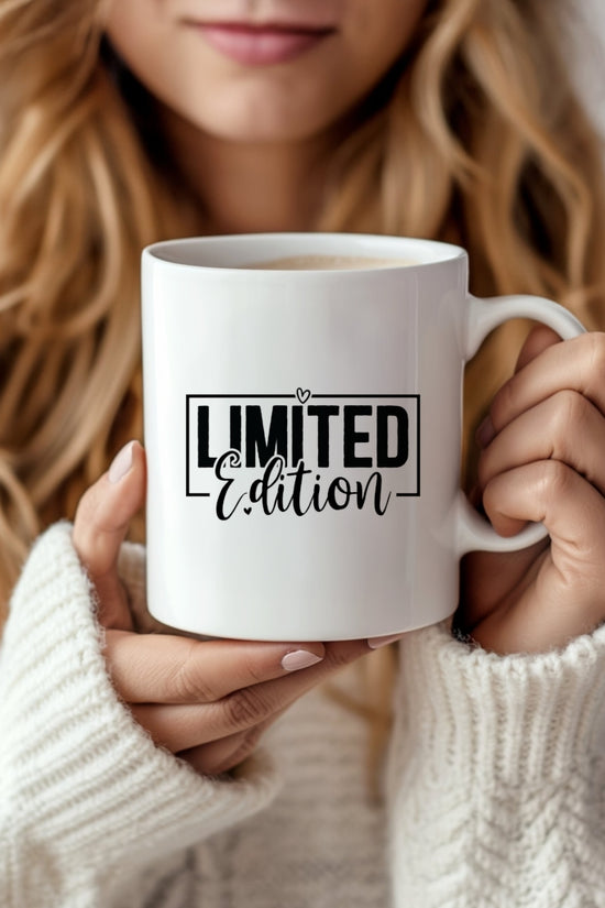 A woman with long wavy hair and a cozy white sweater holds Kreative Kreationz's Limited Edition Mug, featuring the printed text 