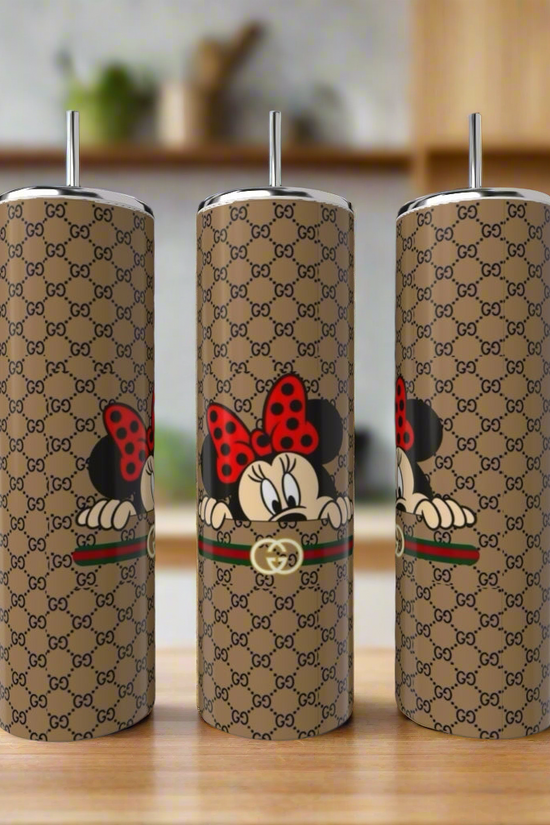 Three Gucci Mickey Mouse 20oz Skinny Tumblers by Kreative Kreationz, in stainless steel with metallic straws and a brown designer pattern featuring Minnie Mouse peeking over a stripe, are shown on wood with a blurred kitchen backdrop.