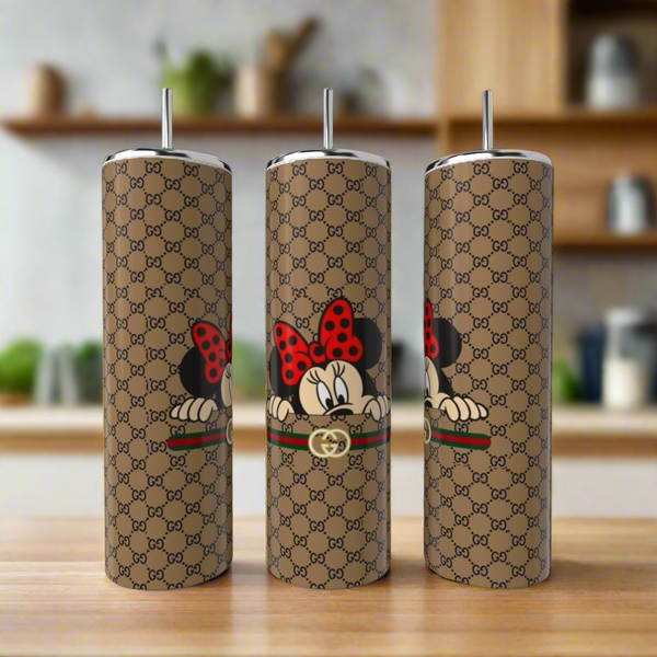 Three Gucci Mickey Mouse 20oz Skinny Tumblers by Kreative Kreationz, in stainless steel with metallic straws and a brown designer pattern featuring Minnie Mouse peeking over a stripe, are shown on wood with a blurred kitchen backdrop.