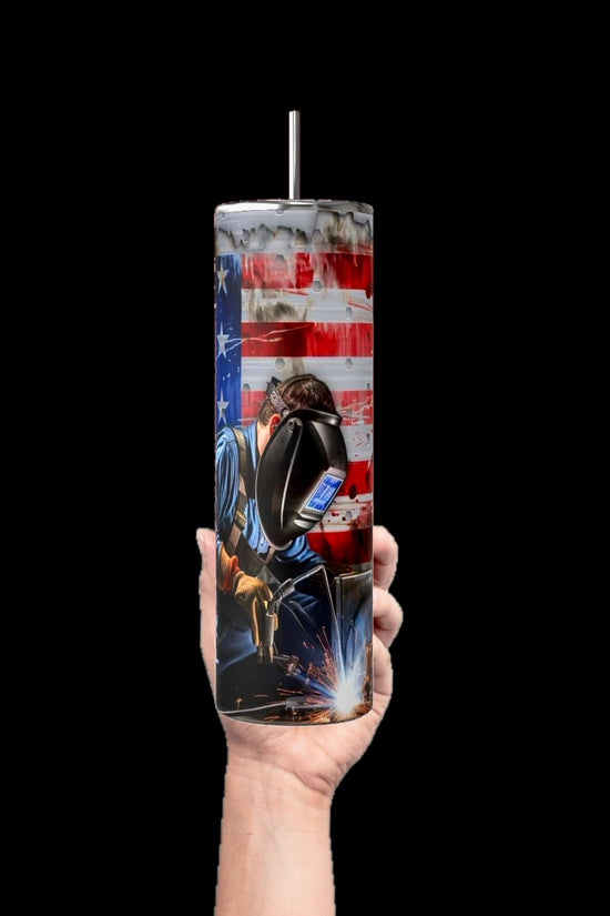 A hand holds the Welders 20oz Tumbler by Kreative Kreationz, featuring an American flag and a welder in a mask with sparks flying. This striking tumbler shines against a solid black backdrop.
