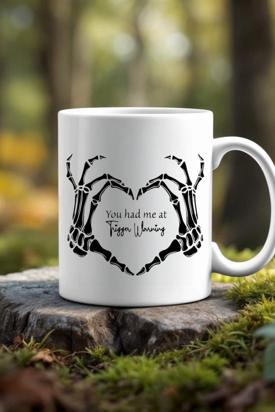 The Trigger Warning Mug by Kreative Kreationz, featuring skeleton hands forming a heart and 