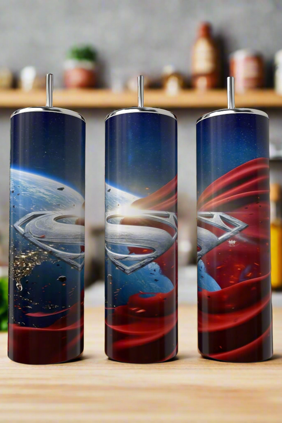 Three Kreative Kreationz Superman 20oz Tumblers with “S” logos are displayed on a kitchen counter, each featuring a stainless steel design inspired by space, Earth, and Superman’s iconic red cape. Blurred jars and utensils add a cozy vibe.