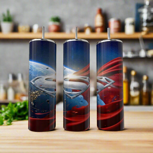 Three Kreative Kreationz Superman 20oz Tumblers with “S” logos are displayed on a kitchen counter, each featuring a stainless steel design inspired by space, Earth, and Superman’s iconic red cape. Blurred jars and utensils add a cozy vibe.