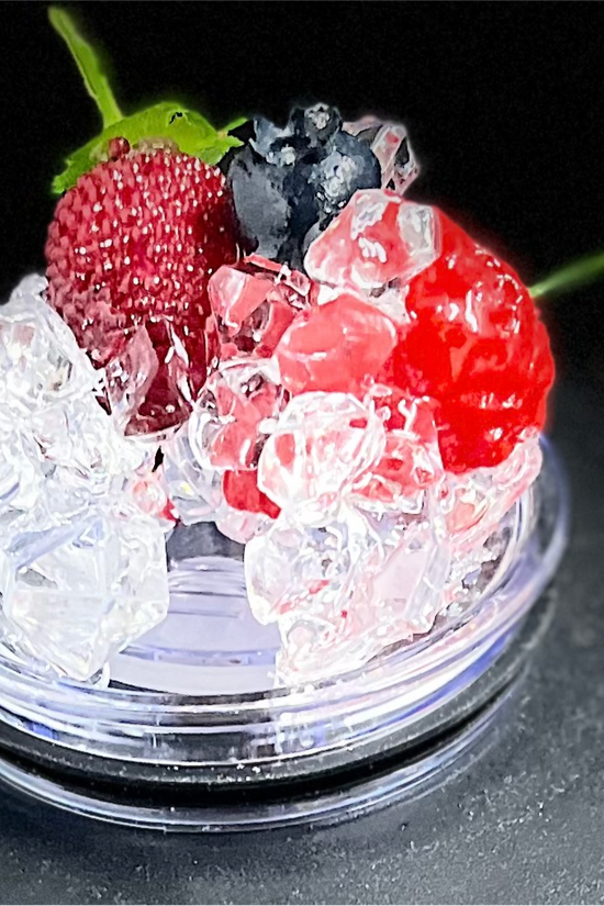 A slice of lime sits atop a pile of crushed ice, elegantly displayed on a small, round, clear platform against a beige background that accentuates the lime and ice. A black strip at the bottom features white text reading 
