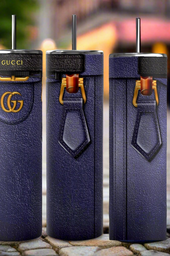Three tall, cylindrical Gucci Diana-inspired purple tumblers from Kreative Kreationz, featuring a leather-like texture, gold Gucci logos, and black straws, stand on a cobblestone street. With durable construction and a 20 oz capacity, the focus remains on these stylish and luxurious cups against the softly blurred background.