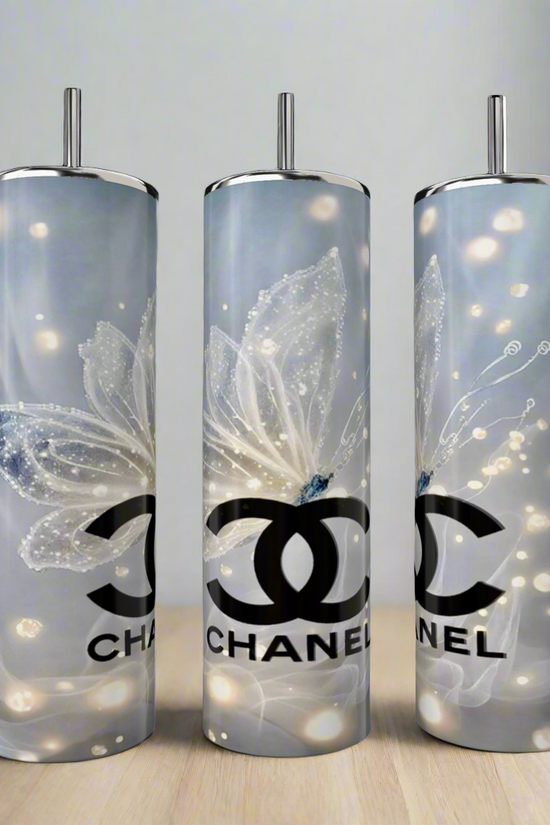 Three Kreative Kreationz CC 20oz Skinny Tumblers with butterfly designs showcase a sleek silver and white palette. Made from double-wall stainless steel, these luxury beverage tumblers rest elegantly on a light wooden surface against a neutral background.