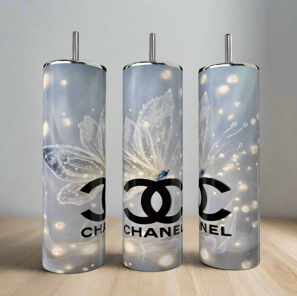 Three Kreative Kreationz CC 20oz Skinny Tumblers with butterfly designs showcase a sleek silver and white palette. Made from double-wall stainless steel, these luxury beverage tumblers rest elegantly on a light wooden surface against a neutral background.