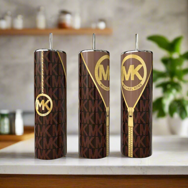 Three tall, brown Peek-a-Boo MK 20oz Tumblers by Kreative Kreationz, featuring gold MK logos and zipper designs, stand on a kitchen counter—a chic stainless steel drinkware set that adds signature elegance to any space.
