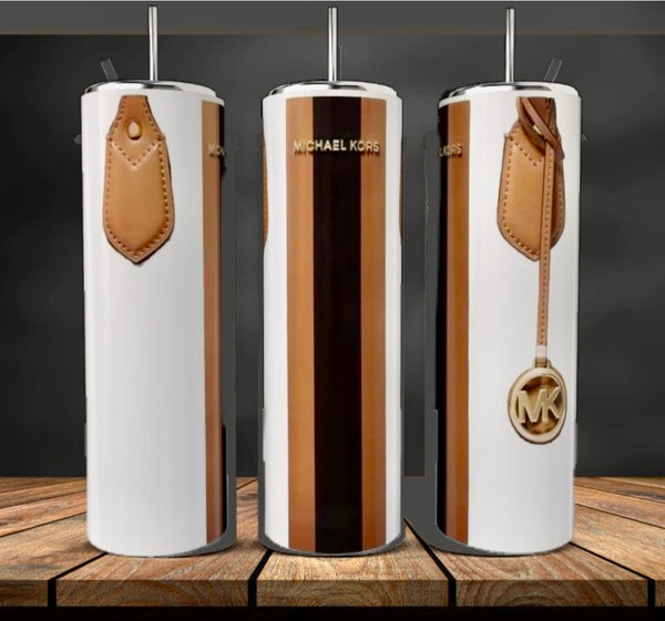 Three tall, glossy Kreative Kreationz MK | White 20oz Tumblers with a metallic gold and white design and brown faux leather details are displayed on a wooden surface against a dark background.