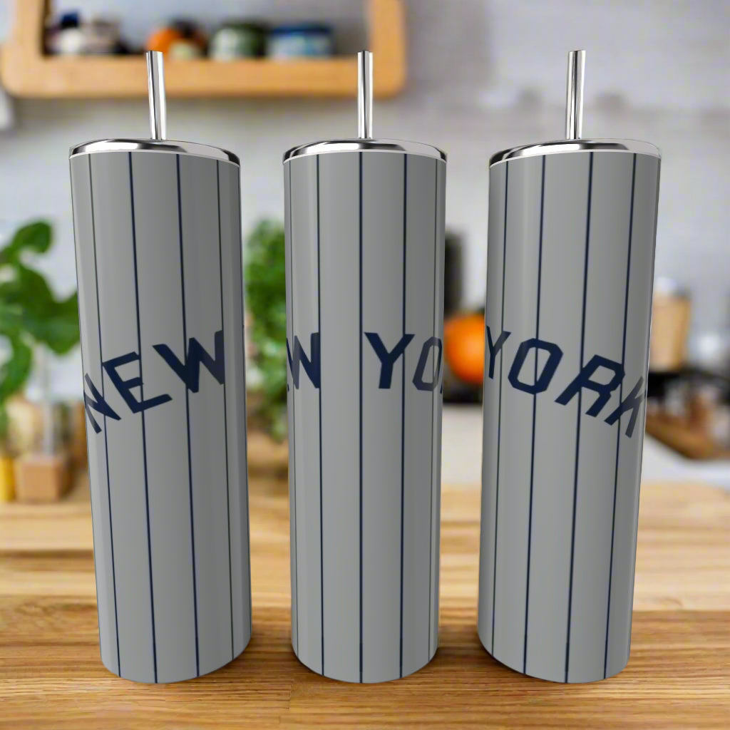 Three tall Kreative Kreationz New York Yankees Grey 20oz Tumblers with silver finish and blue "NEW YORK" lettering stand on a wooden counter—an ideal set for Yankees fans.