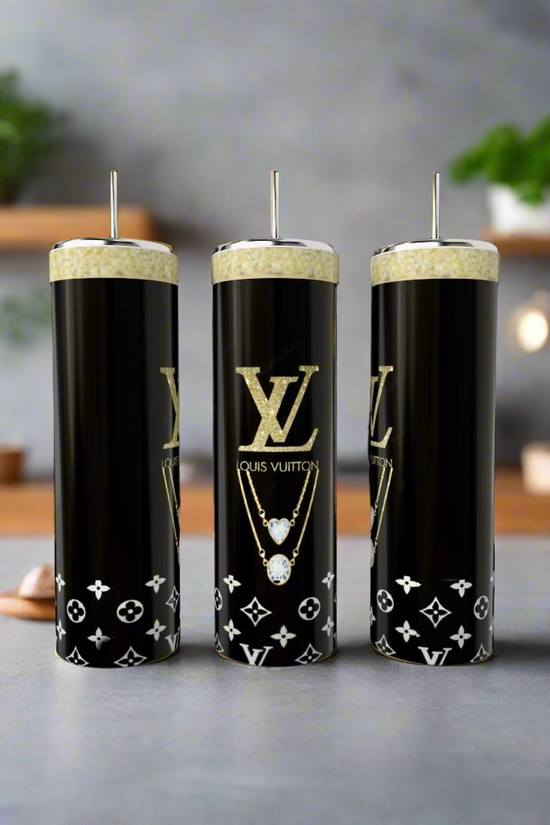 Three luxury-logo tall black candles with white patterns are set next to Kreative Kreationz's Louis Vuitton Purse 20oz stainless steel tumbler in a modern setting, with blurred shelves holding plants and kitchen items in the background.