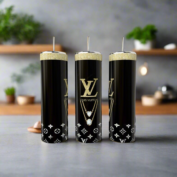 Three luxury-logo tall black candles with white patterns are set next to Kreative Kreationz's Louis Vuitton Purse 20oz stainless steel tumbler in a modern setting, with blurred shelves holding plants and kitchen items in the background.