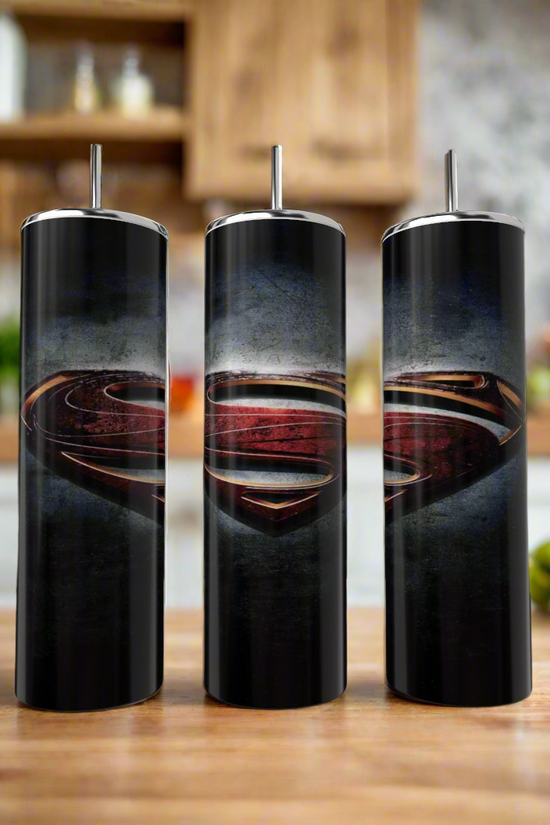 Three Kreative Kreationz Superman Smokey 20oz Tumblers with straws and a bold dark Superman logo are displayed on a wooden kitchen counter, with shelves and produce softly blurred in the background.