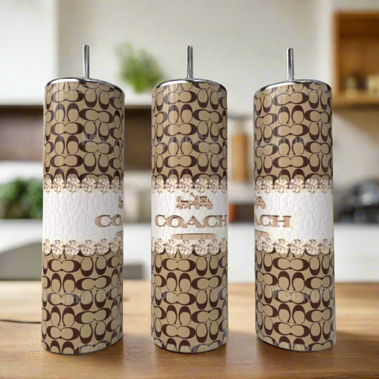 Three Kreative Kreationz Coach Brown 20oz Skinny Tumblers, featuring brown and beige logo patterns with white bands, sit on a wooden surface, adding stylish luxury to the modern kitchen.