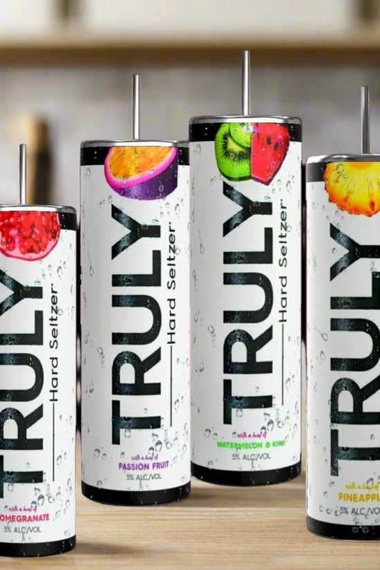 Four cans from the Truly Hard Seltzer 20oz Skinny Tumbler Collection by Kreative Kreationz are displayed on a wooden surface. The flavors showcased are pomegranate, passion fruit, pineapple, and another indistinguishable fruit. The sleek, tall cans feature refreshing water droplets on their design. Enhance your drinking experience with a reusable straw for an eco-friendly touch.