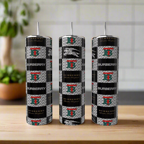 Three Burberry Inspired 20oz Tumblers by Kreative Kreationz, featuring black, silver, and red patterns with metallic straws, stand on a wooden surface against a blurred kitchen background—luxurious drinkware style.