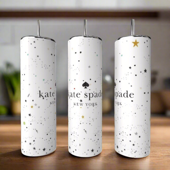 Three white Kreative Kreationz Kate Spade Sparkle 20oz Skinny Tumblers with silver lids and straws, adorned with stars and dots, are shown on a wooden surface in a softly blurred kitchen—stylish luxury drinkware for your home.