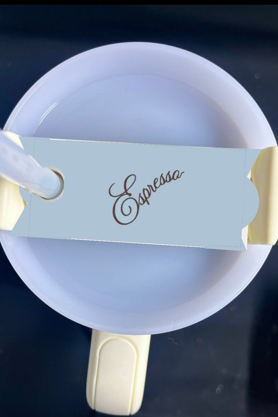 Top view of a beige coffee cup with a white rim. A small thin card with the word 