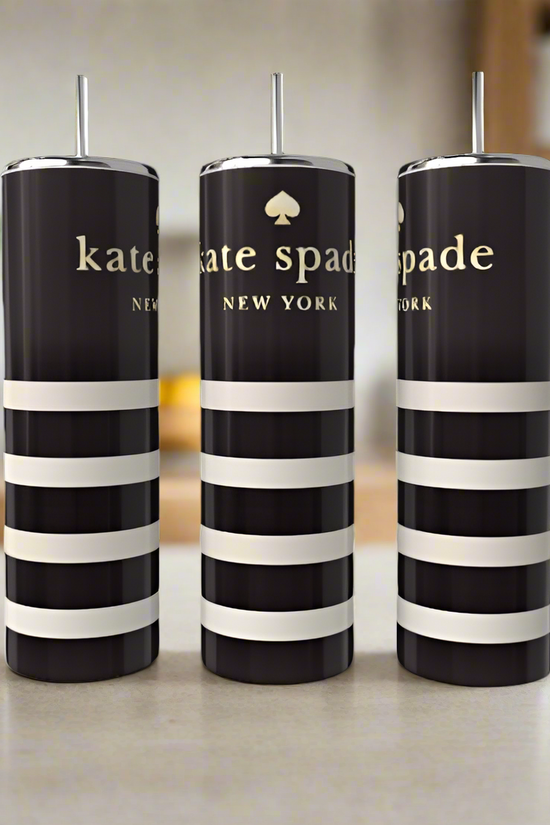 Three Kate Spade 20oz Skinny Tumblers from Kreative Kreationz, featuring black and white stripes with silver lids and straws, sit elegantly on a countertop. The blurred kitchen background, with plants and shelves, enhances the drinkware's allure.