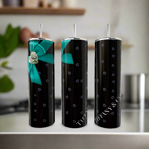 Three sleek, black Kreative Kreationz Tiffany Hearts 20oz Tumblers display small blue heart patterns. One features a large blue bow with a silver heart. Made from eco-friendly stainless steel, the words "Tiffany & Co." shine on two against a blurred kitchen backdrop.