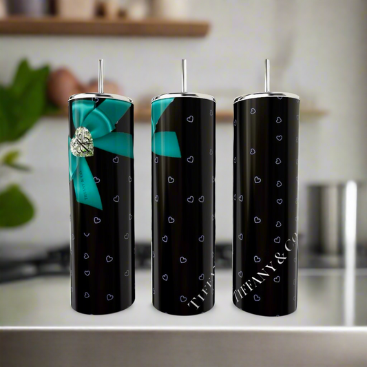 Three sleek, black Kreative Kreationz Tiffany Hearts 20oz Tumblers display small blue heart patterns. One features a large blue bow with a silver heart. Made from eco-friendly stainless steel, the words "Tiffany & Co." shine on two against a blurred kitchen backdrop.