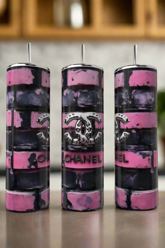 Three Kreative Kreationz Chanel Brick 20oz Tumblers with straws showcase a pink and black brick pattern plus the iconic logo, styled as luxury drinkware on a kitchen counter with shelves and potted plants in the background.