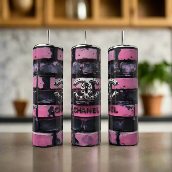 Three Kreative Kreationz Chanel Brick 20oz Tumblers with straws showcase a pink and black brick pattern plus the iconic logo, styled as luxury drinkware on a kitchen counter with shelves and potted plants in the background.