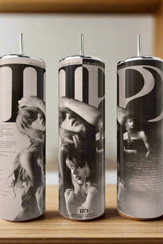 Three tall, cylindrical Kreative Kreationz TTPD 20oz Tumblers feature luxury-inspired designs with black-and-white images of women in hats. Elegantly placed on a wooden surface, they blend beautifully with a blurred background of shelves and plants.
