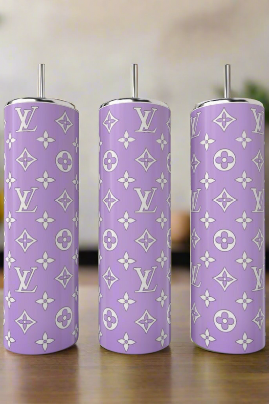 Three tall lavender tumblers from Kreative Kreationz’s LV Inspired 20oz Tumbler Collection, each with metal straws and white luxury patterns, sit on a wooden surface with greenery and soft lighting in the background.