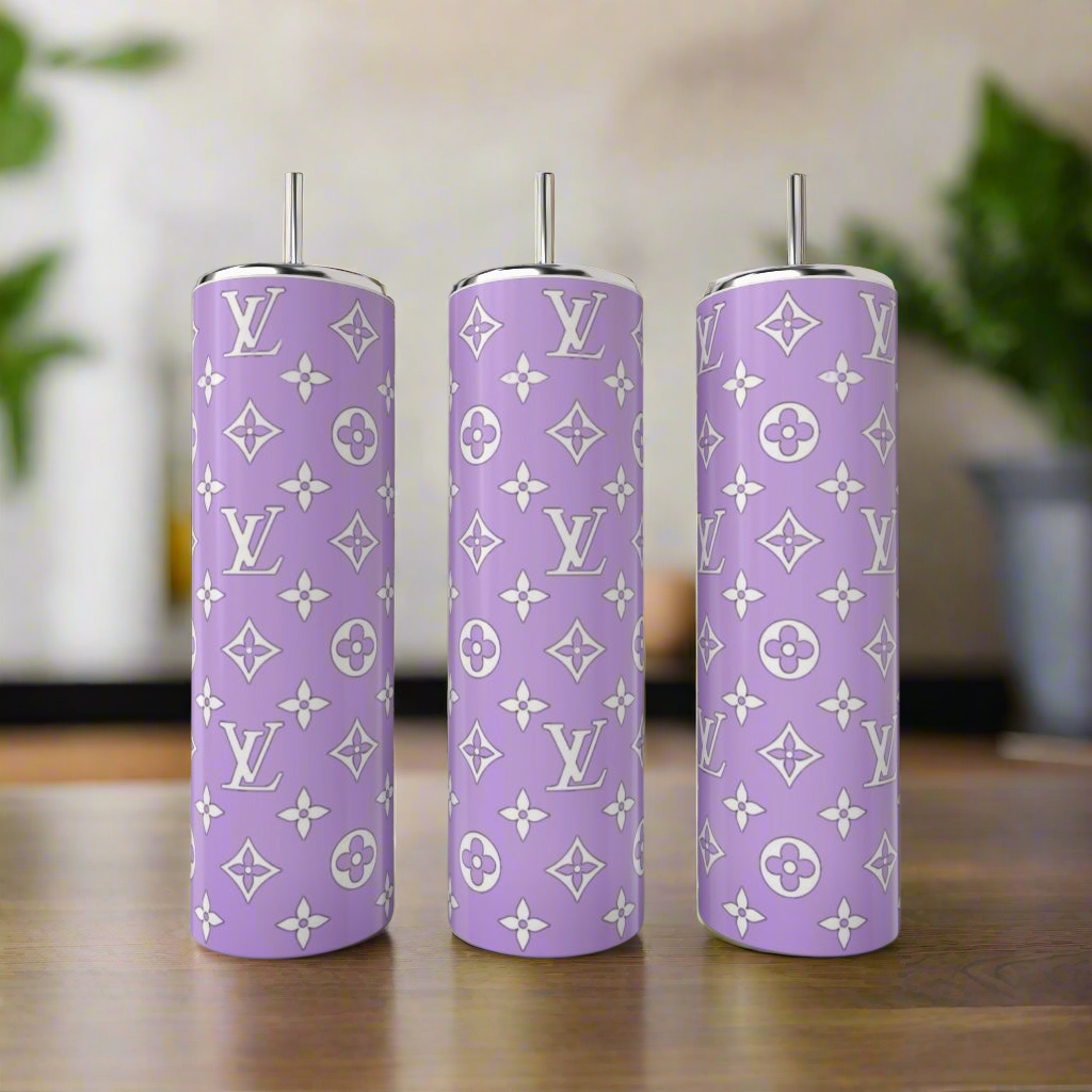 Three tall lavender tumblers from Kreative Kreationz’s LV Inspired 20oz Tumbler Collection, each with metal straws and white luxury patterns, sit on a wooden surface with greenery and soft lighting in the background.