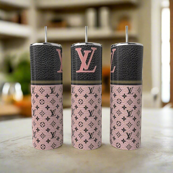Three Kreative Kreationz LV Blush Pink 20oz Tumblers with metal straws are displayed on a countertop. Featuring a luxury-inspired monogram design, each stainless steel tumbler adds style to your drinkware. A blurred kitchen is in the background.