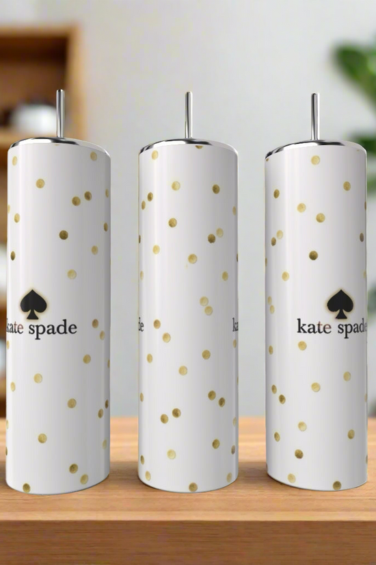 Three tall, white Kreative Kreationz Kate Spade Tumblers with gold polka dots and logos stand on a wooden surface, complemented by a blurred kitchen and green plant in the background for a stylish look.