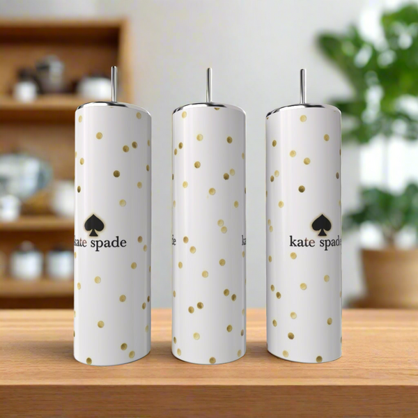Three tall, white Kreative Kreationz Kate Spade Tumblers with gold polka dots and logos stand on a wooden surface, complemented by a blurred kitchen and green plant in the background for a stylish look.