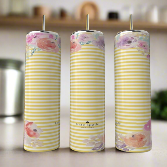 Three tall, striped candles with pastel floral patterns stand on a blurred kitchen counter beside a stylish Kreative Kreationz Kate Spade Spring 20oz Skinny Tumbler.