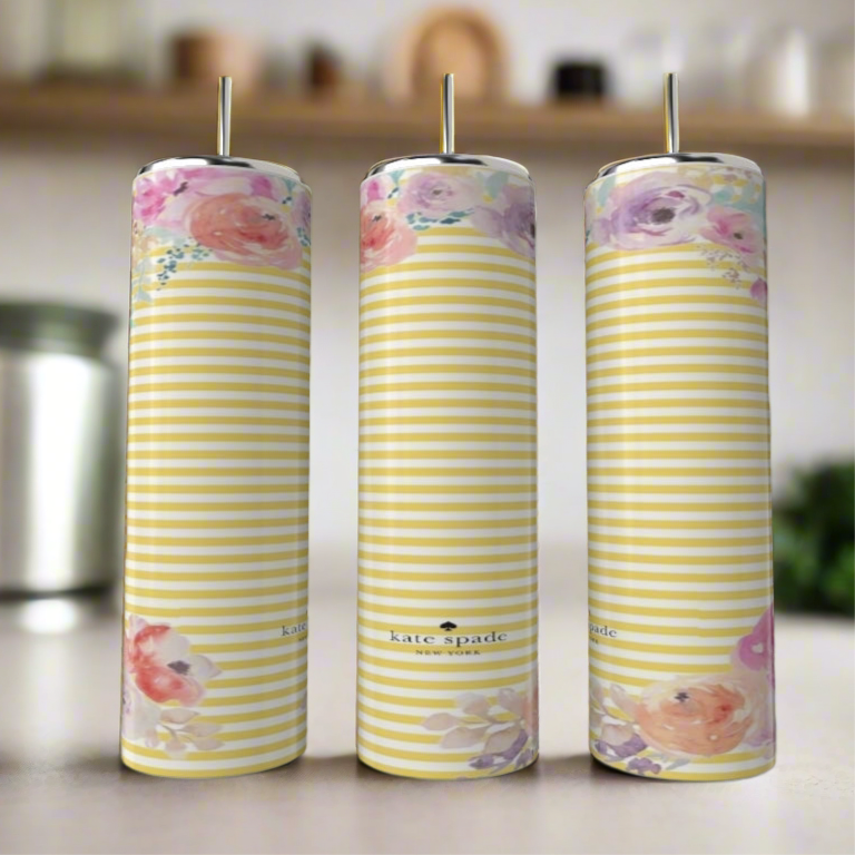 Three tall, striped candles with pastel floral patterns stand on a blurred kitchen counter beside a stylish Kreative Kreationz Kate Spade Spring 20oz Skinny Tumbler.
