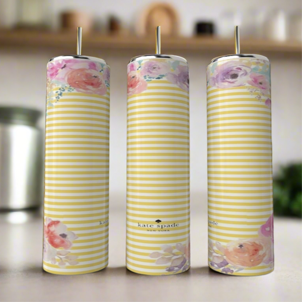 Three tall, striped candles with pastel floral patterns stand on a blurred kitchen counter beside a stylish Kreative Kreationz Kate Spade Spring 20oz Skinny Tumbler.